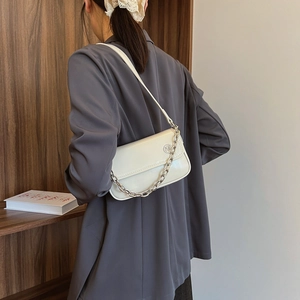 Detail of white leather shoulder bag featuring silver chain links and metal hardware on model