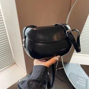 Détail d'un sac selle noir brillant avec rivets métalliques et bandoulière en cuir