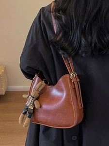 Brown vintage leather bucket bag with cute rabbit pendant shown on a model in black coat