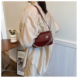 Detailed view of burgundy leather shoulder bag featuring bold silver chain and metallic logo