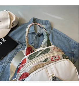 Gros plan sur la poignée renforcée et les broderies florales du sac à dos blanc femme