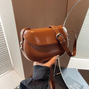 Détail du sac selle en cuir marron avec rivets argentés et bandoulière réglable en lumière