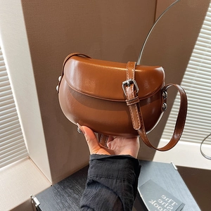Détail du sac selle en cuir mat marron avec boucle métallique et rivets latéraux