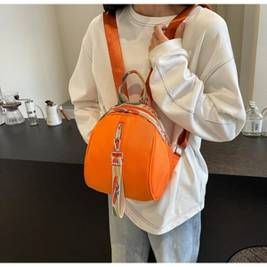 Gros plan d'un mini sac à dos orange avec lanières florales sur une tenue blanche