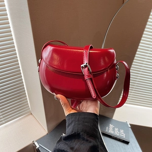 Détail du sac selle en cuir verni rouge foncé avec boucles et rivets argentés