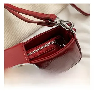 Detail of red glossy leather bag featuring silver round buckle and metallic zipper closure