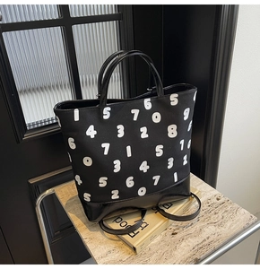 Détail d'un sac cabas en toile noire avec imprimés chiffres et poignées en cuir