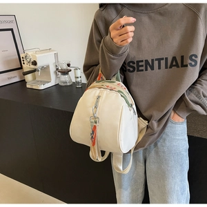 Gros plan d'un sac à dos en nylon beige avec poignée en sangle jacquard colorée et zip argenté