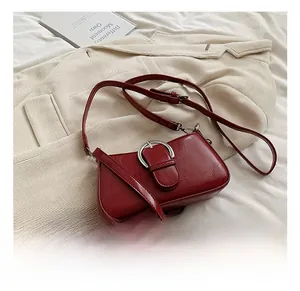 Close-up of wine red PU leather crossbody bag with silver oval metal buckle on a blazer