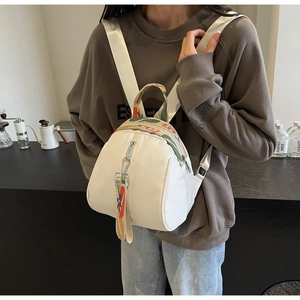 Détail sac à dos beige forme coquille avec poignée tissée et ruban sur sweat marron