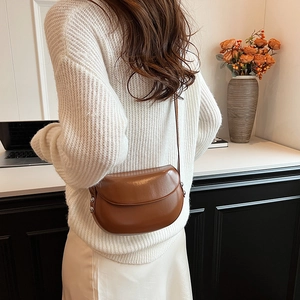 Sacoche marron en cuir portée avec un pull blanc et une jupe en soie dans un décor cosy