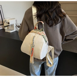 Détail d'un mini sac à dos beige avec des sangles tissées à fleurs sur la poignée