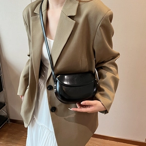 Détail d'un sac selle en cuir noir brillant avec des rivets argentés et une bandoulière fine