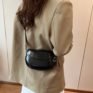Gros plan sur un sac besace noir en cuir verni porté par un mannequin en blazer brun