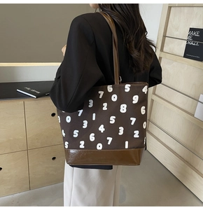 Détail du grand sac cabas en toile marron avec chiffres imprimés sur l'épaule du mannequin