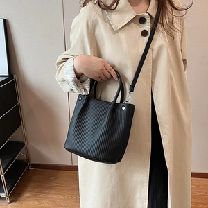 Dettaglio di una borsa a secchiello plissettata nera abbinata a un trench beige per l'autunno
