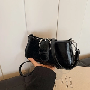 Detail of glossy black faux leather shoulder bag featuring a silver metal buckle