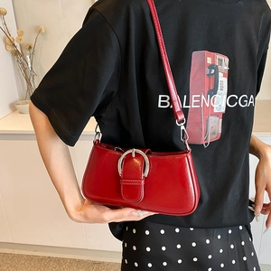 Detail of red glossy patent leather underarm bag featuring a prominent silver round buckle
