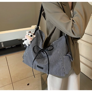 Vista laterale di una grande borsa tote a righe con fiocco in pelle e ciondolo a mucca