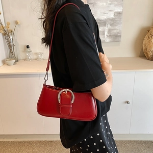 Detail of dark red high-gloss underarm bag with large silver metal oval buckle