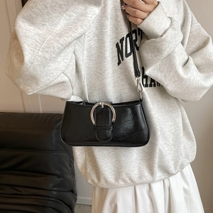 Detail of black leather underarm bag with silver round buckle shown on a model