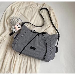 Dettaglio borsa tote in tela a righe blu con fiocco nero e ciondolo a forma di mucca