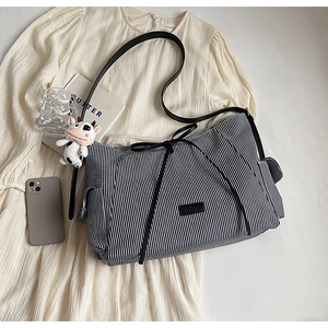 Dettaglio di una borsa tote in tela a righe blu con fiocco nero e ciondolo a mucca peluche