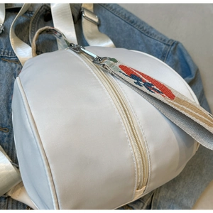 Détail d'un sac à dos blanc en nylon avec poignée tissée colorée et zip argenté