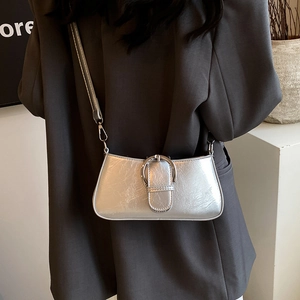 Detail of silver metallic crossbody bag featuring glossy crinkled texture and wide buckle decoration