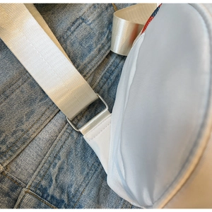 Détail du sac à bandoulière en nylon blanc avec coutures renforcées et boucles argentées