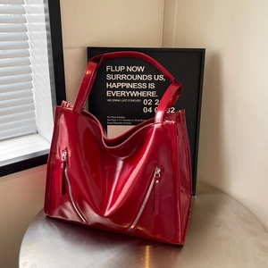 Close-up of a large red glossy tote bag featuring decorative silver zippers on the front
