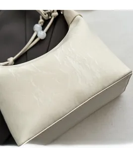 Detail einer cremefarbenen Handtasche mit Marmortextur, Knotengurt und Perlendekor