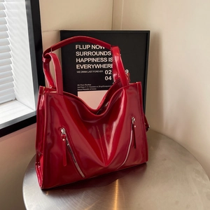 Detail of red glossy tote bag featuring decorative metal zippers and shiny patent finish