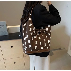 Detail of coffee canvas tote with white numbers, drawstring bow, and leather bottom