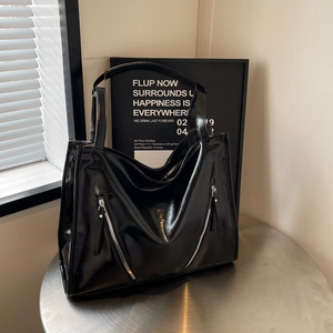 Detail of glossy black tote bag featuring decorative diagonal zippers on the front