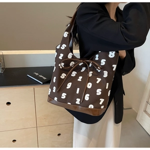 Detailed side view of a large brown canvas tote with white numbers and bow detail