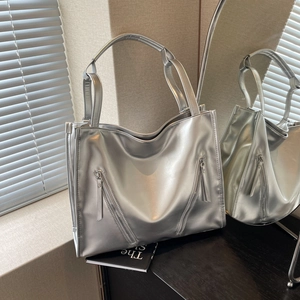 Detail of silver metallic tote bag with decorative zippers on a dark wooden surface