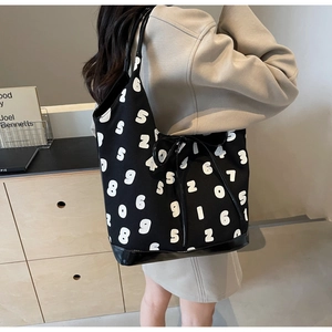 Detail of a black canvas tote bag featuring white number prints and a glossy leather base