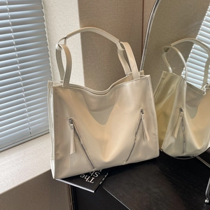 Close-up of cream glossy tote bag with symmetrical diagonal zippers and shoulder straps
