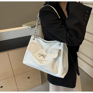 Close-up of a white tote bag featuring a silver bow buckle and elegant chain shoulder strap