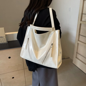 Detail of a large cream patent leather tote bag with side gussets and zipper accents