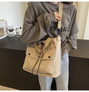 Détail du sac cabas en toile beige avec poches avant et cordons rayés dans un café