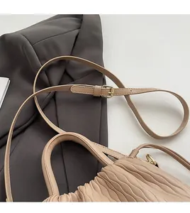 Détail du sac seau matelassé beige avec bandoulière réglable sur un blazer sombre