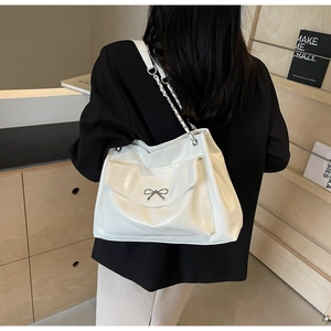 Detail of white glossy tote bag with metal bow and chain strap on a model shoulder