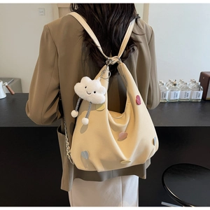 Zaino in tela beige con toppe a cuore e ciondolo di peluche indossato da modella