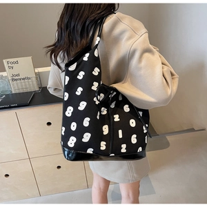 Model showing a large black canvas bucket bag with white number prints and shiny leather trim