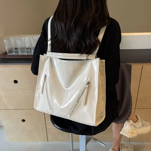 Detail of glossy off-white tote bag with dual front zipper pockets on female model