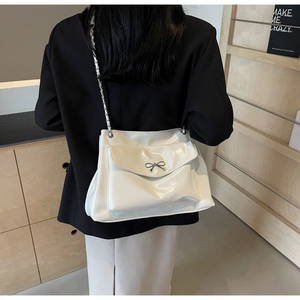 Close-up of white patent leather tote with silver bow and metal chain strap detail