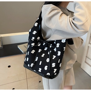 Detail of canvas shoulder bag with white numeric print and black decorative bow strap