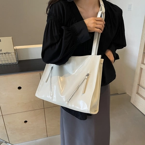 Detail of a creamy white glossy tote bag with dual zippers and wide shoulder strap